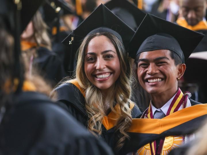 Two students wearing caps and gowns pose for photo at Commencement